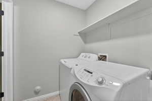 Dedicated laundry area featuring a white wall shelf, light gray wall paint, and white baseboards