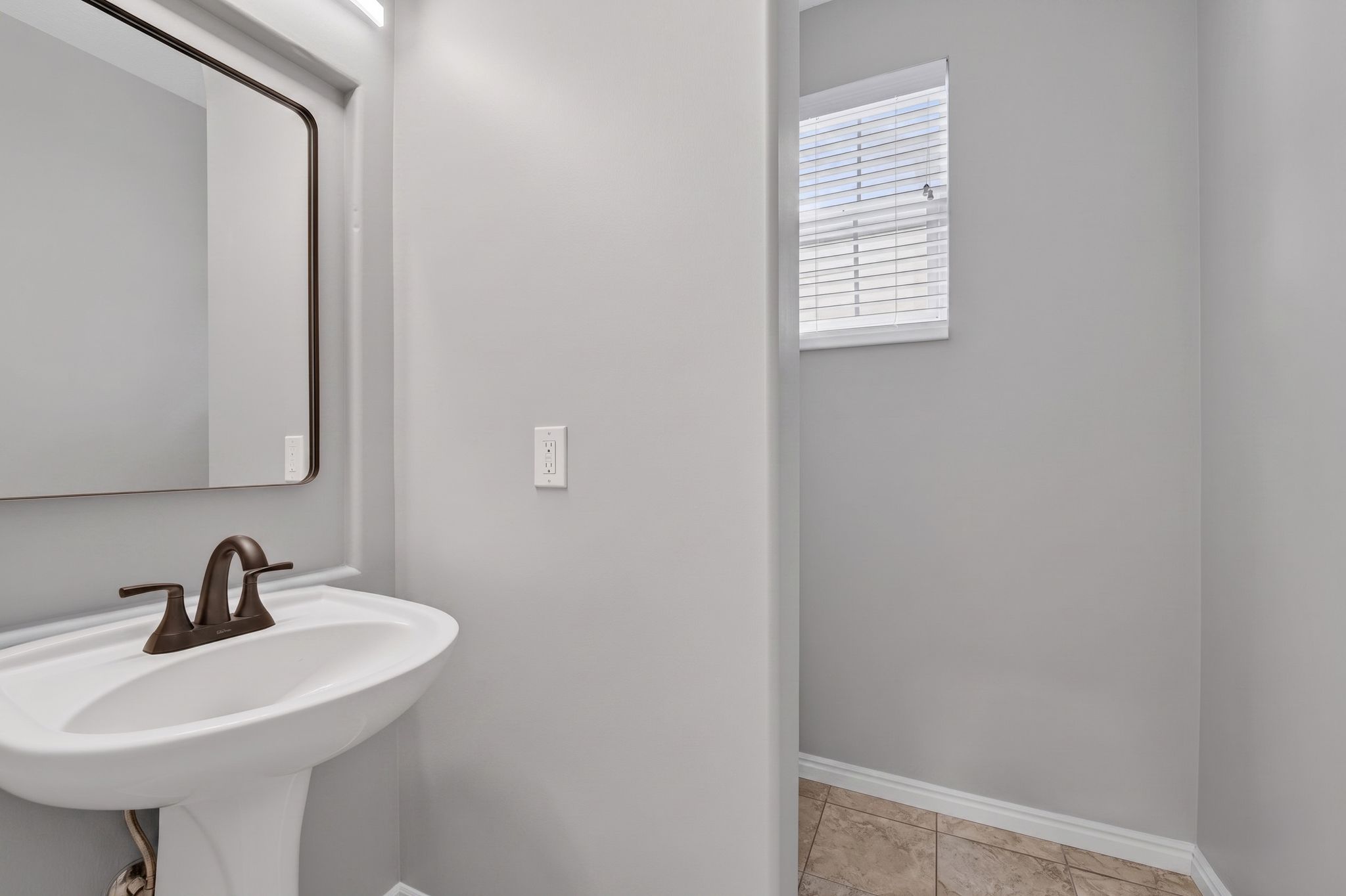 Pedestal sink with bronze-finish faucet, rectangular mirror, and overhead lighting