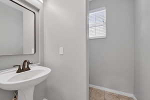 Pedestal sink with bronze-finish faucet, rectangular mirror, and overhead lighting