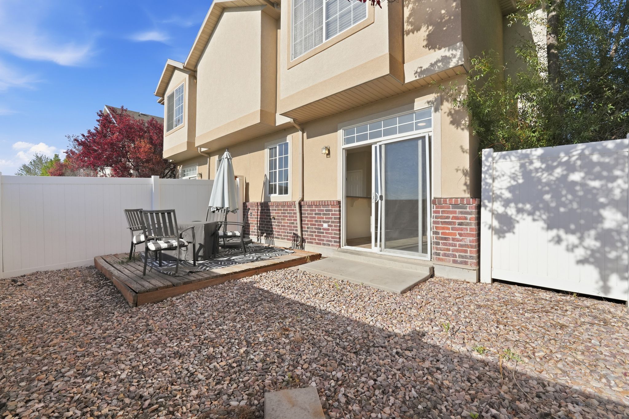 Private outdoor patio featuring a wooden deck, sliding glass door access, and a rock-covered yard