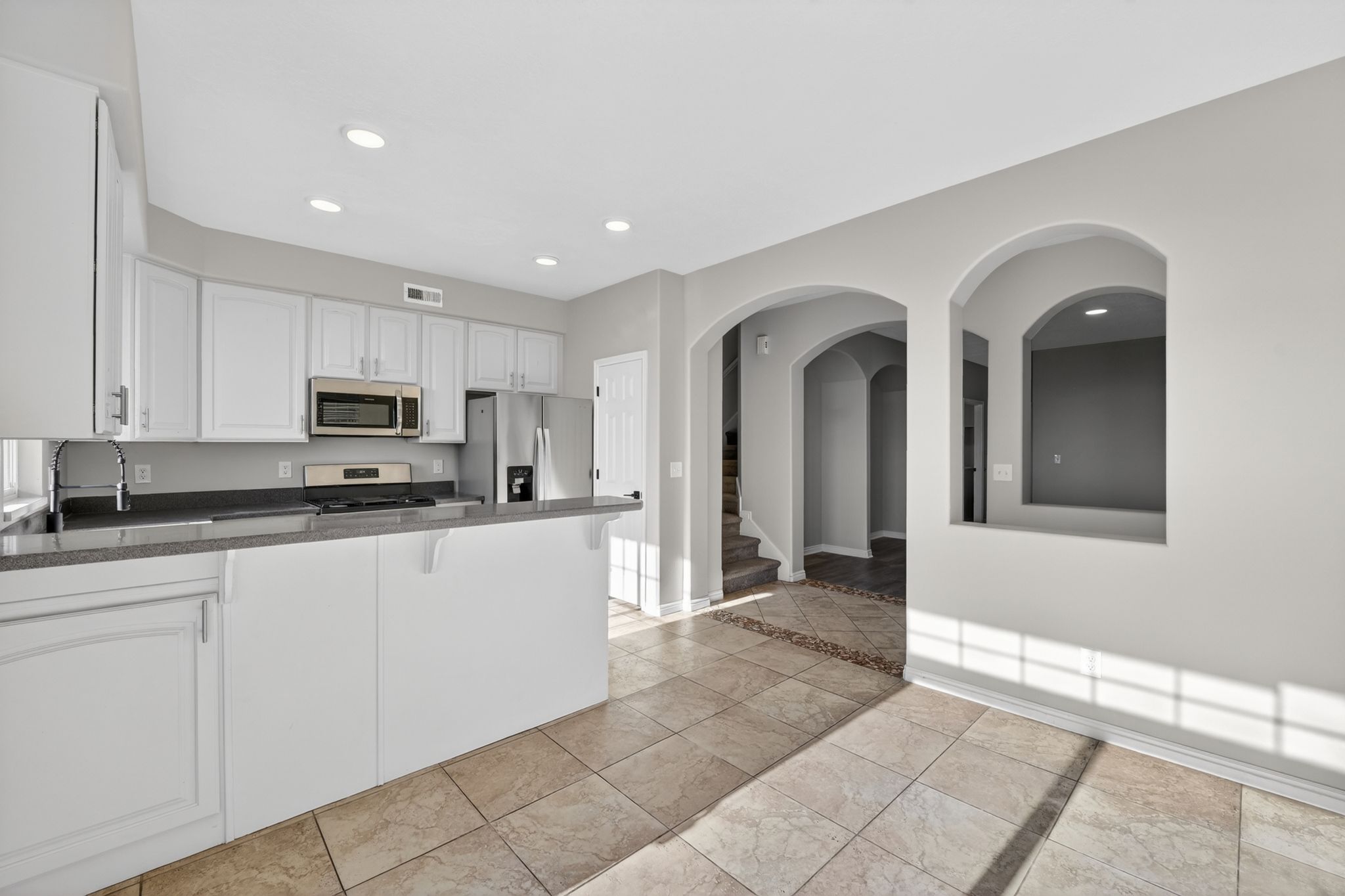 Open-concept kitchen with recessed lighting, white cabinetry, dark countertops, and stainless steel appliances