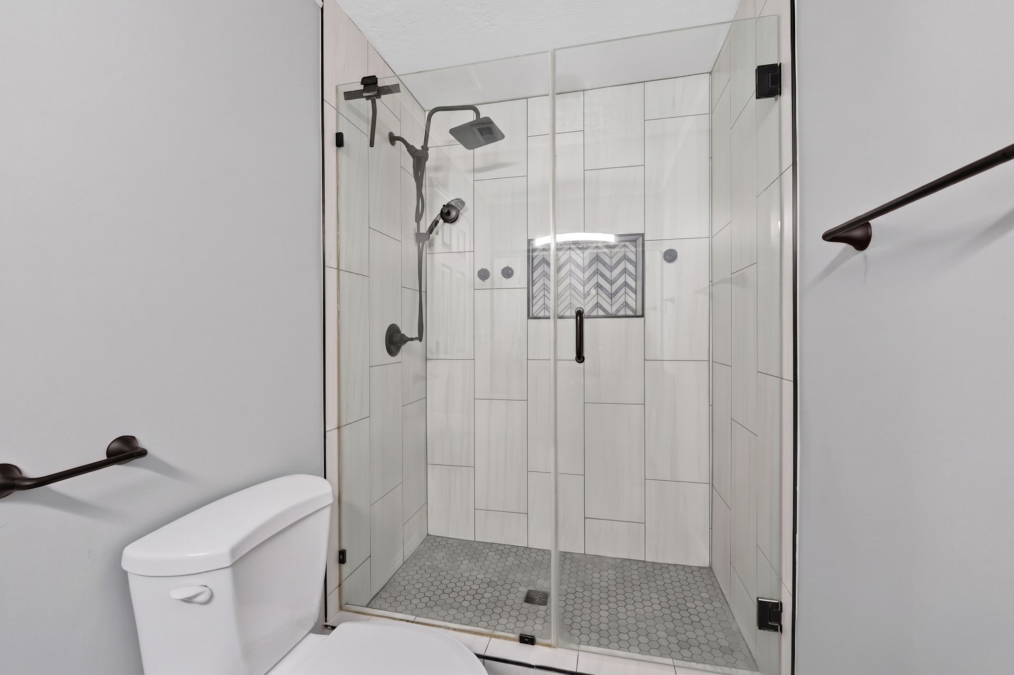 Glass-enclosed shower featuring a rainfall showerhead, handheld sprayer, and dark bronze fixtures