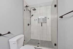 Glass-enclosed shower featuring a rainfall showerhead, handheld sprayer, and dark bronze fixtures