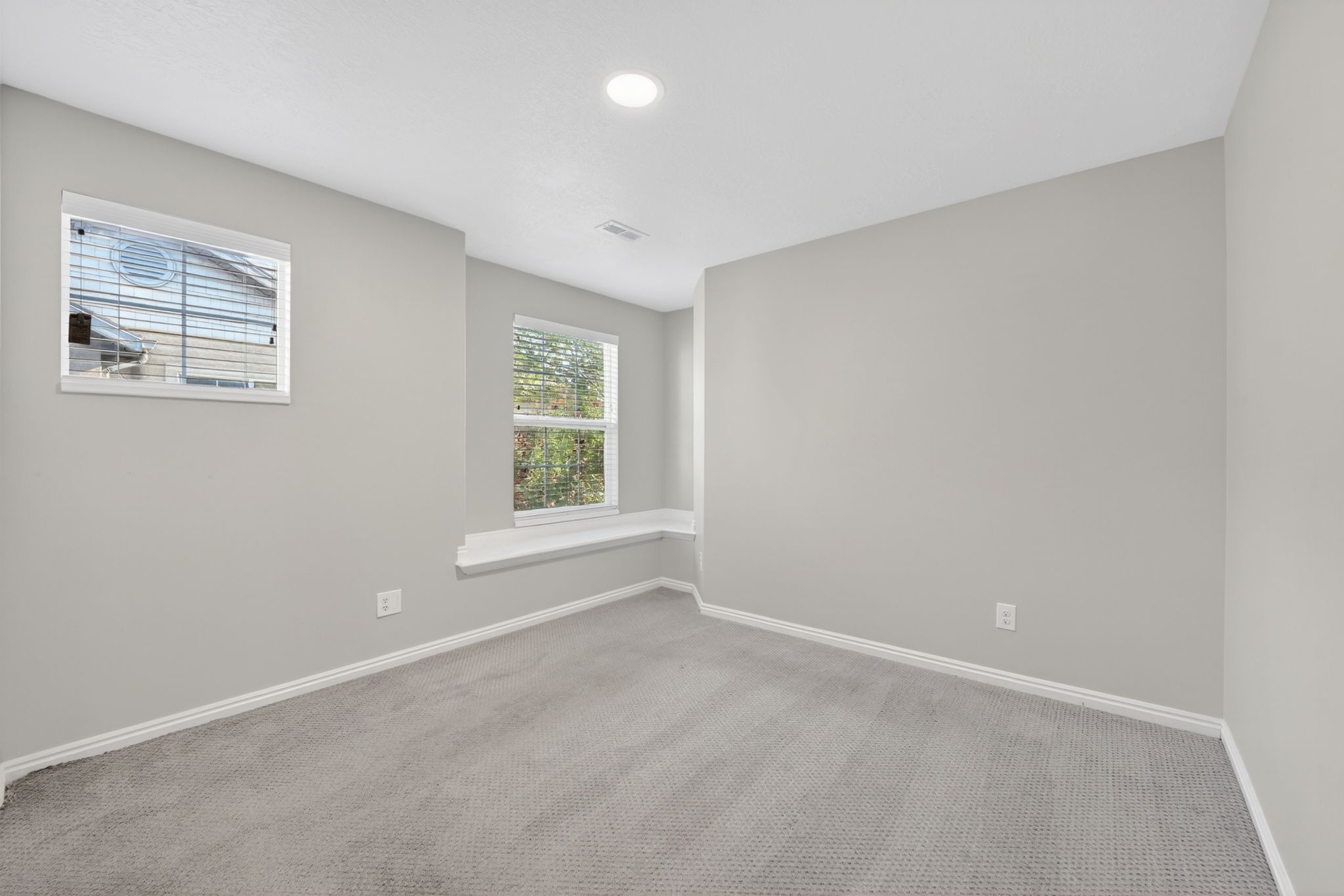 Carpeted room featuring light gray walls, two windows, and a built-in window bench