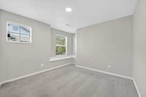 Carpeted room featuring light gray walls, two windows, and a built-in window bench
