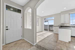 Entry foyer featuring a white paneled door with transom window, tile flooring, and arched architectural details