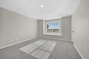 Recessed lighting illuminates a neutral-toned room with light gray walls and gray carpeting
