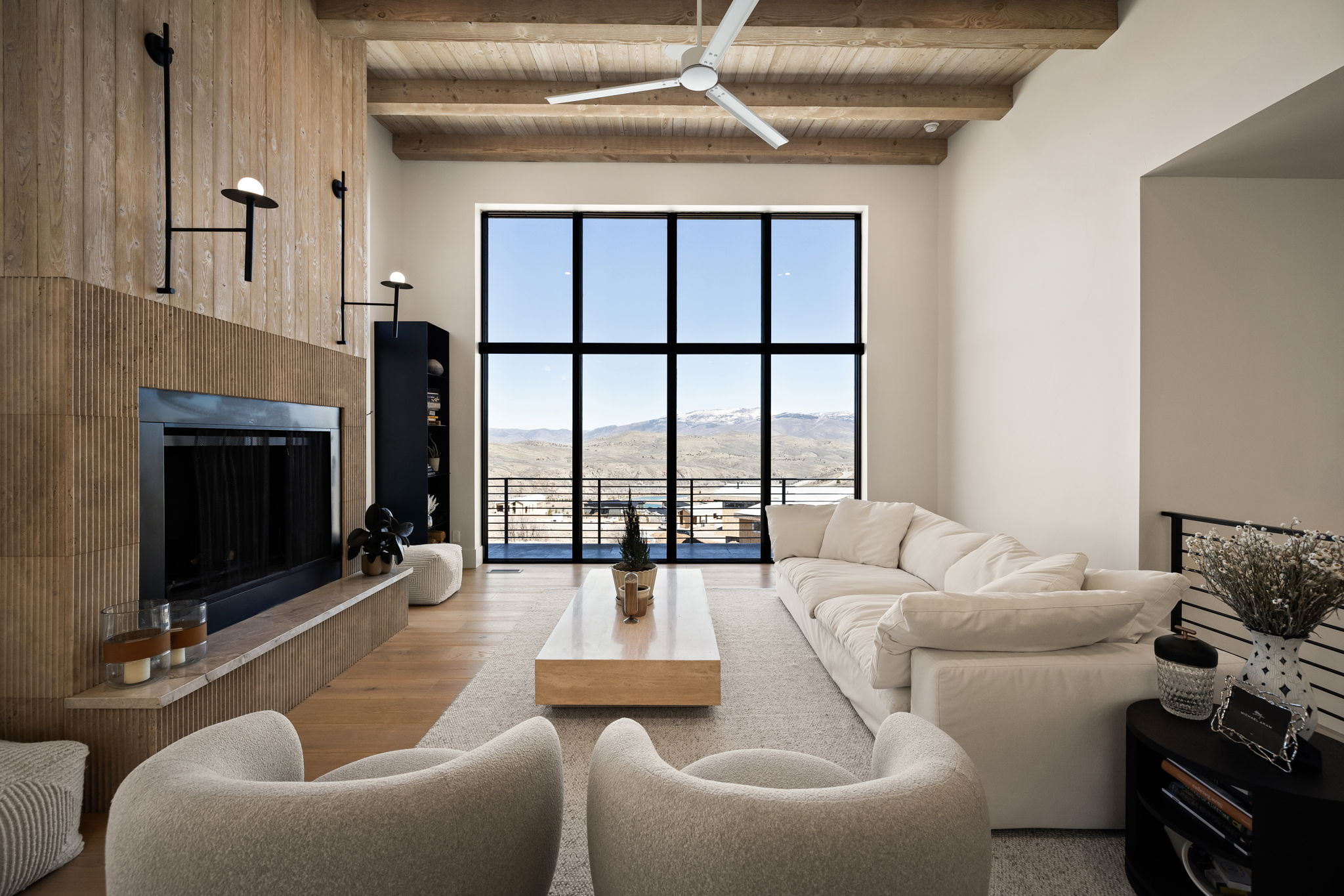 Floor-to-ceiling windows with mountain scenery, vaulted wood-beam ceiling, wood-finish wall paneling, built-in fireplace with stone surround, and wood-finish flooring