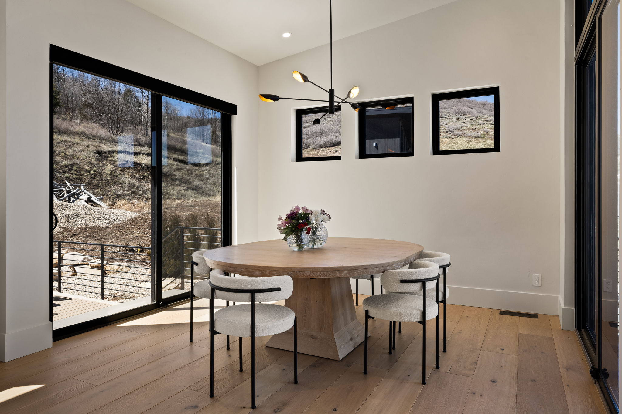 Spacious dining area featuring wood-finish flooring, a contemporary chandelier, and a large sliding glass door opening to an outdoor deck with metal railings