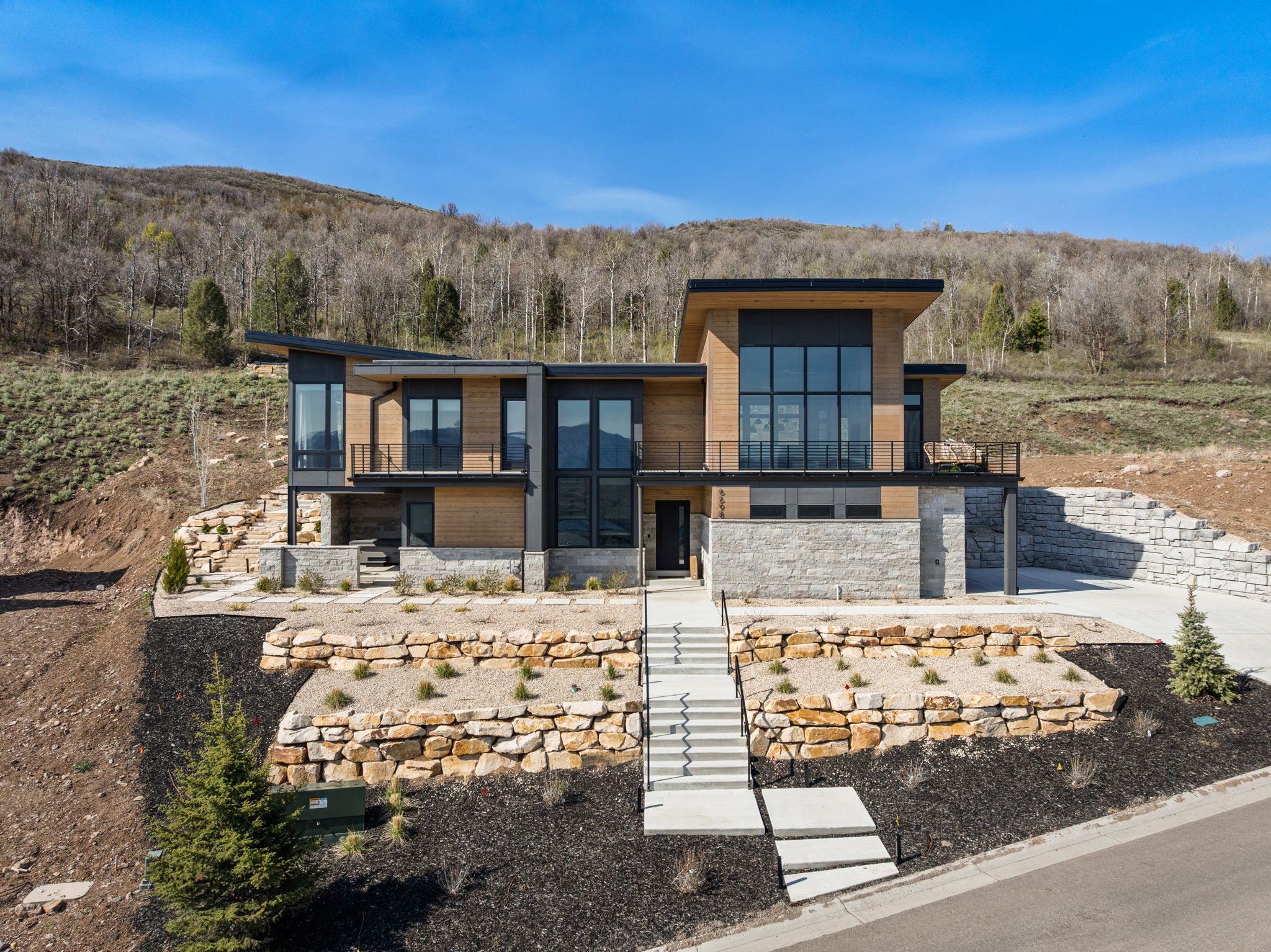 Modern architectural design featuring expansive glass panels, wood-finish siding, and stacked stone accents