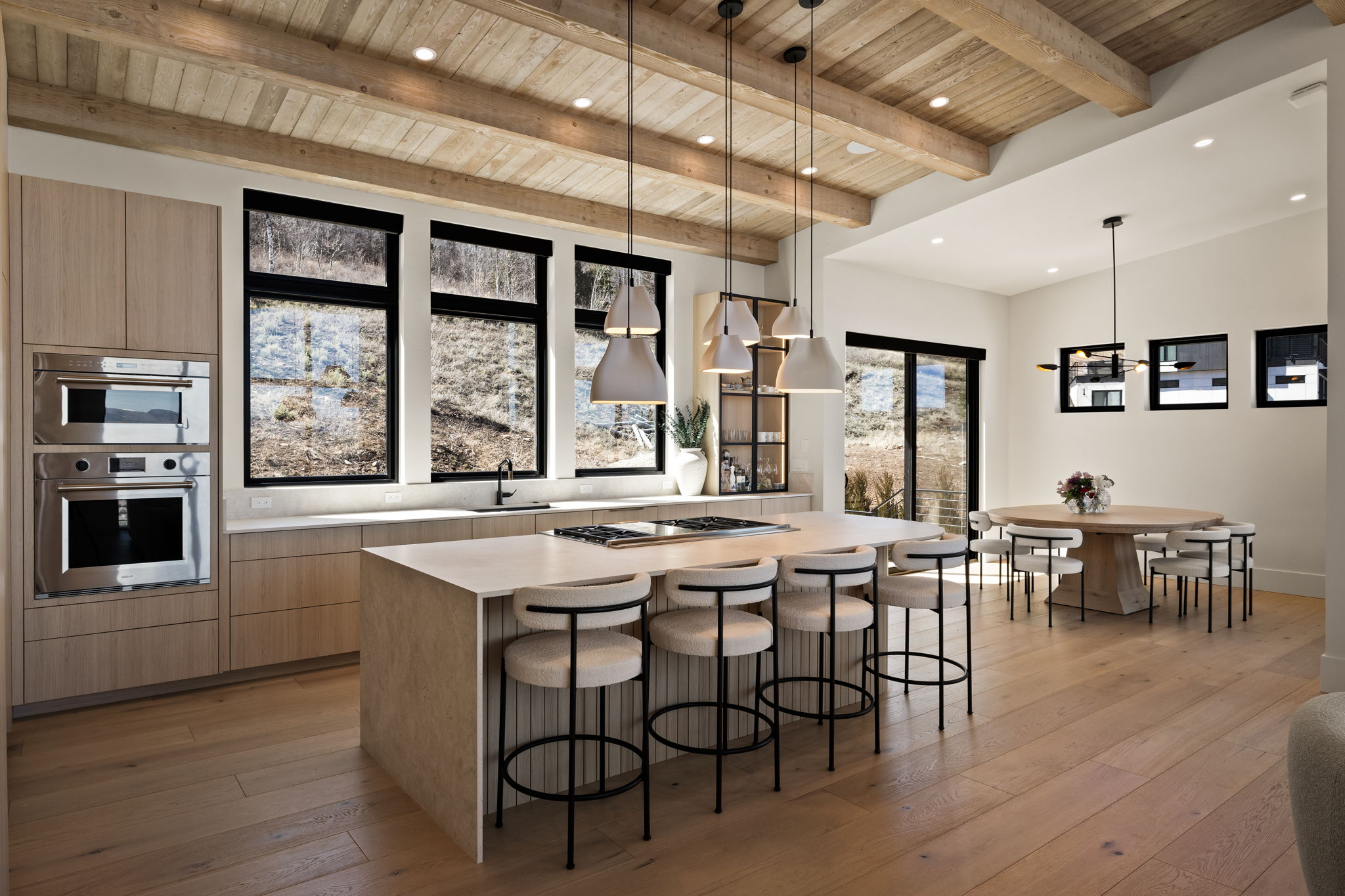 Open concept kitchen and dining area featuring a wood-beam vaulted ceiling, wood-finish flooring, and built-in stainless steel double ovens