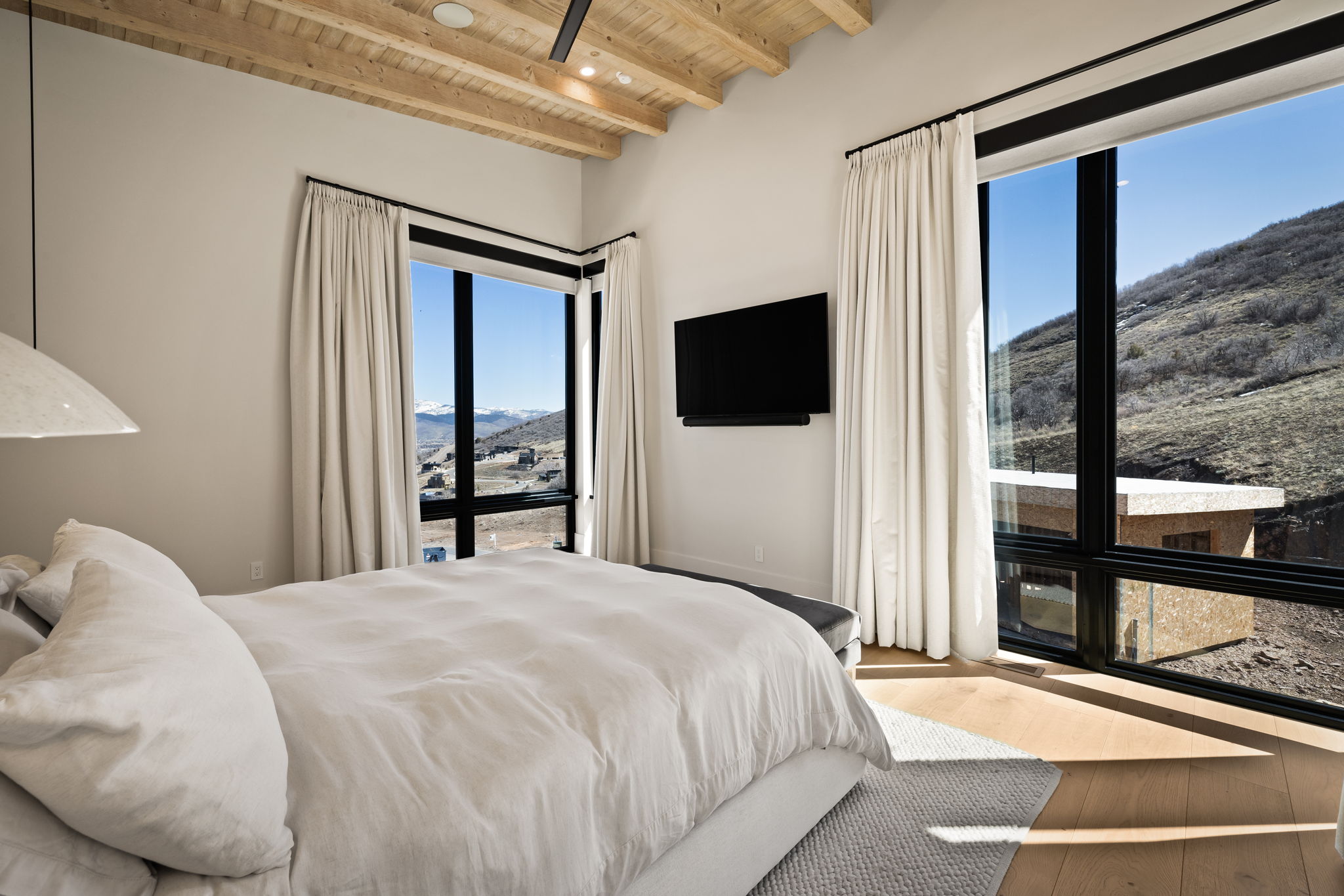 Bedroom featuring abundant natural light, a wood-finish vaulted ceiling with exposed beams, wood-finish flooring, and large windows with black framing