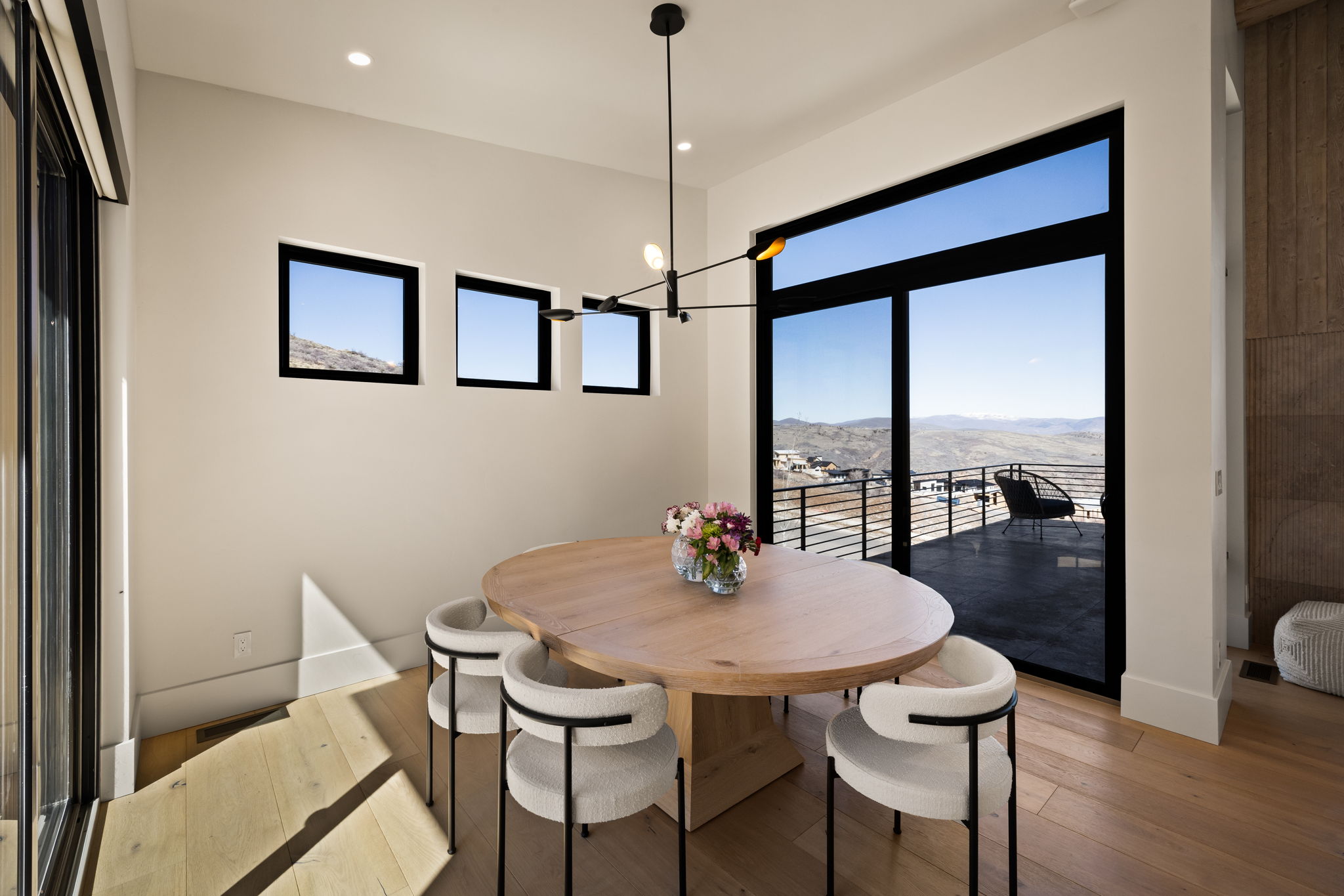 Spacious dining area featuring a light wood dining table, wood-finish flooring, and a contemporary chandelier