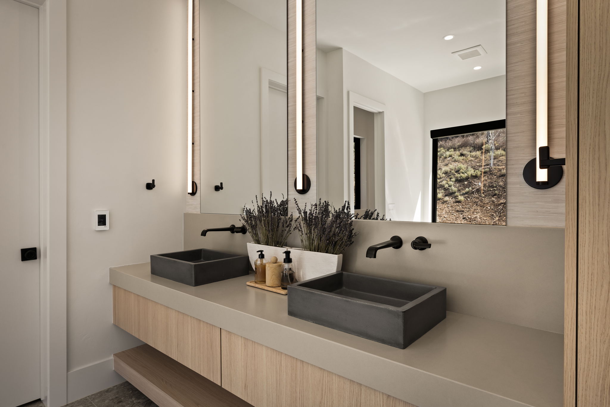 Dual vessel sinks set atop a light-toned countertop, featuring a wood-finish vanity with integrated storage