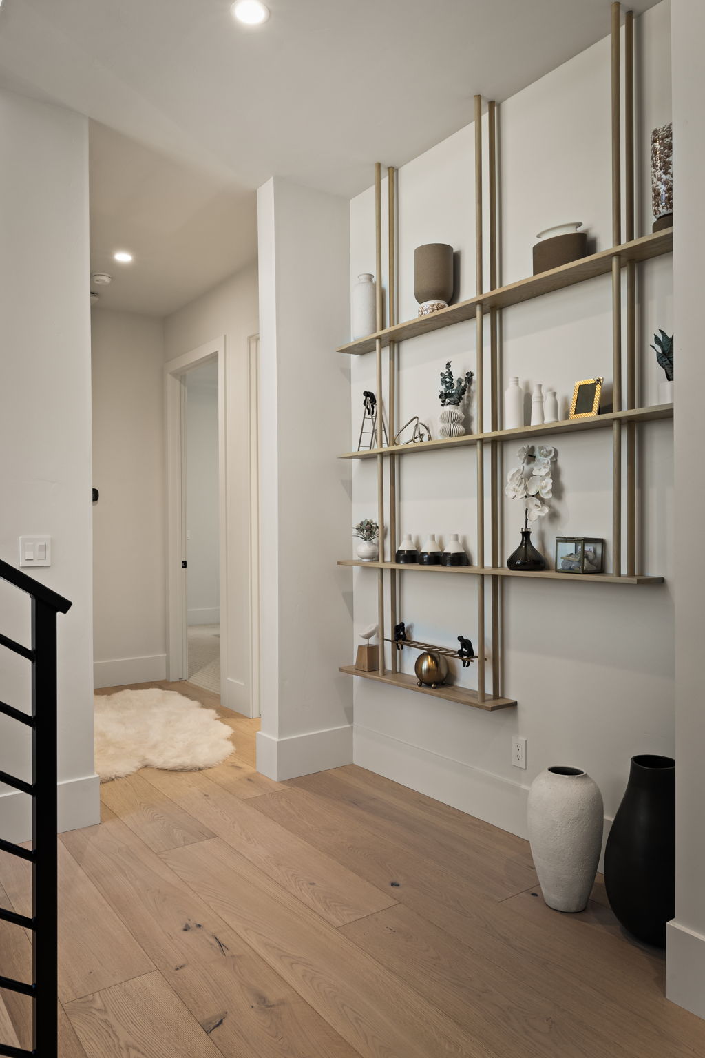 Hallway featuring light wood-finish flooring, recessed lighting, a modern built-in shelving unit with gold-tone accents, and white baseboards