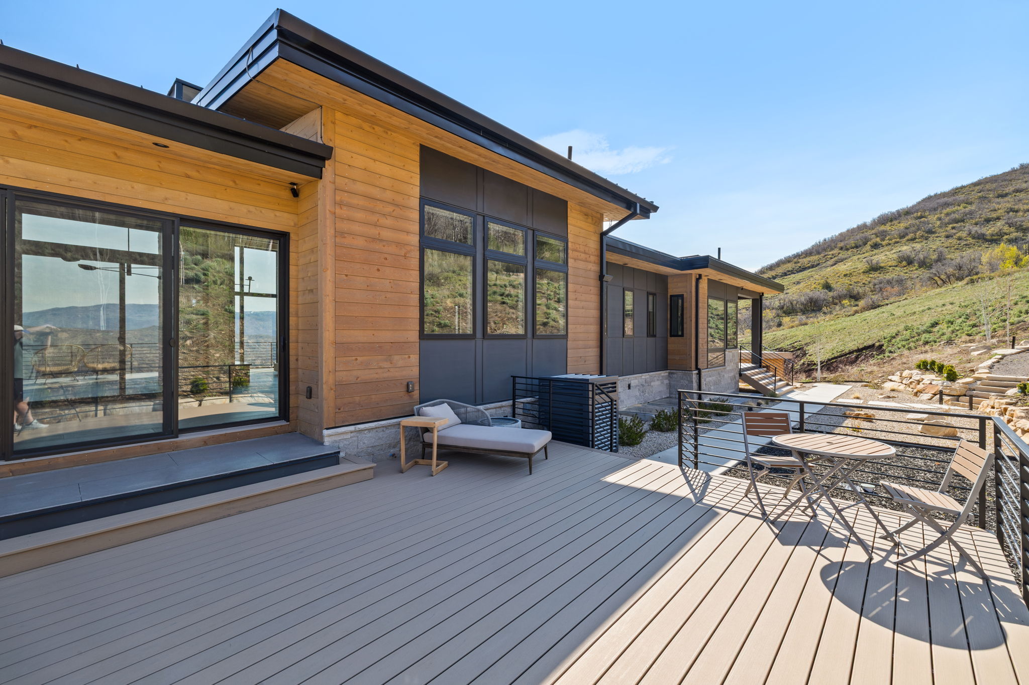 Expansive composite deck featuring a cable railing system, multiple sliding glass doors, and a natural wood-siding exterior