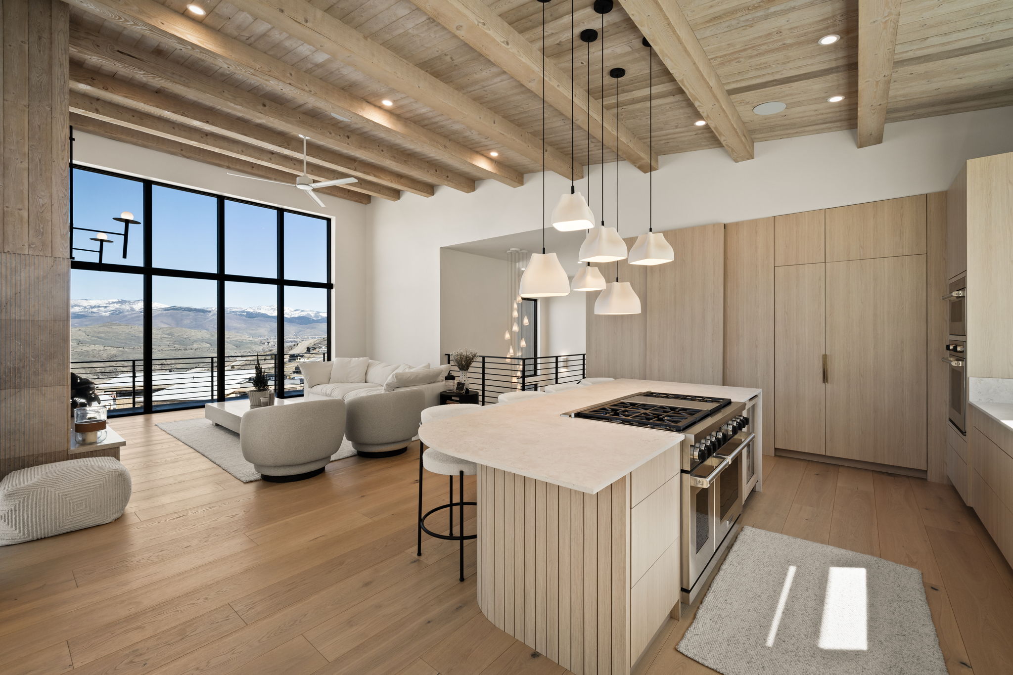 Great room featuring expansive window walls, vaulted wood-beamed ceilings, light wood-finish flooring, and a stone fireplace