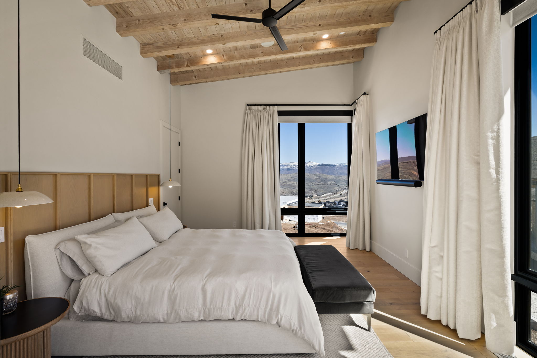 Bedroom featuring a vaulted wood-beam ceiling, ceiling fan, wide plank wood-finish flooring, and large windows with mountain scenery