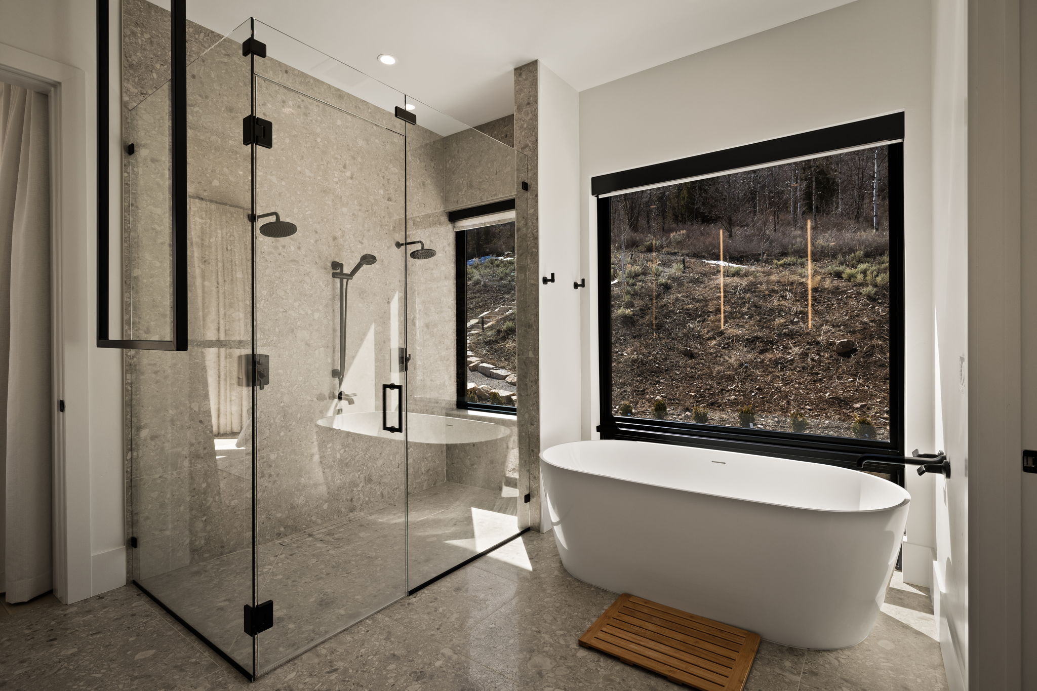 Modern bathroom featuring an expansive glass-enclosed shower with dual shower heads, a freestanding soaking tub, large format floor and wall tiles, and an oversized picture window