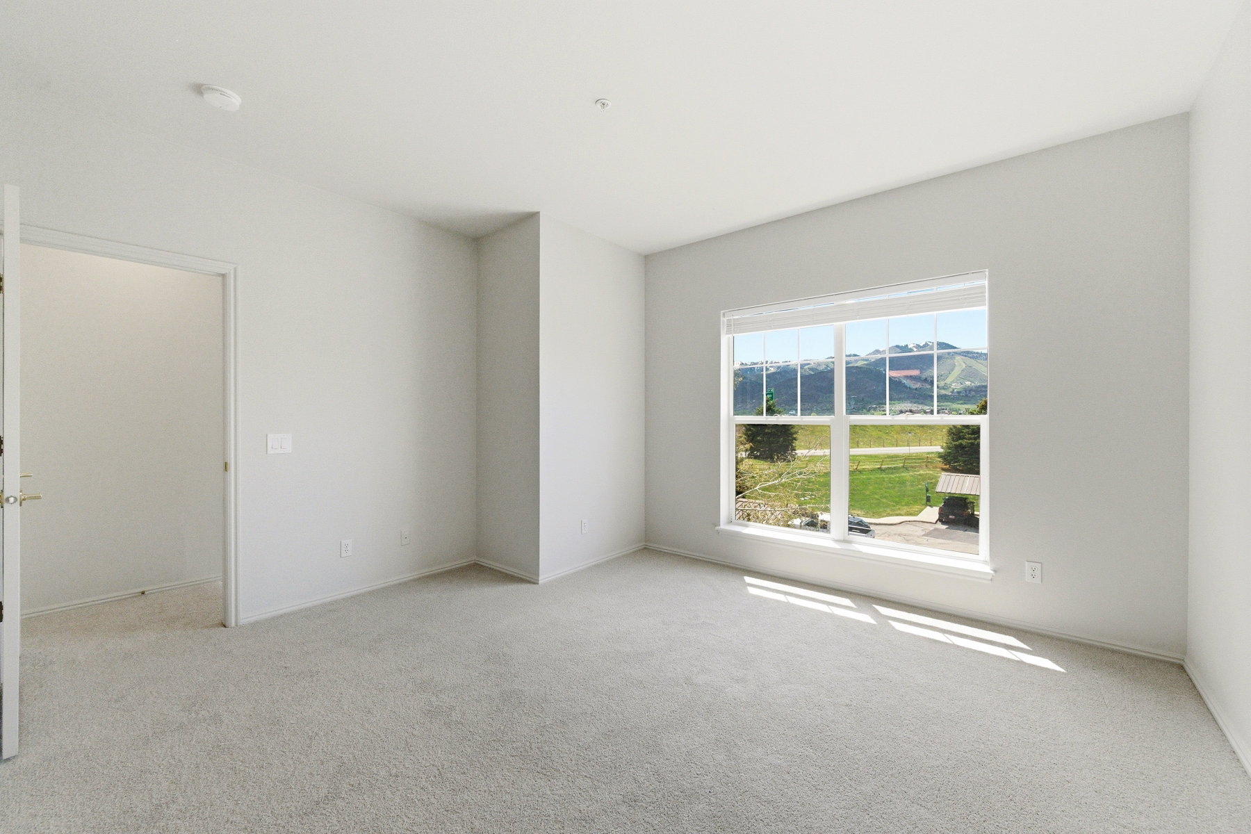 Spacious room featuring neutral carpeting, light-toned walls, and a large window with a mountain backdrop