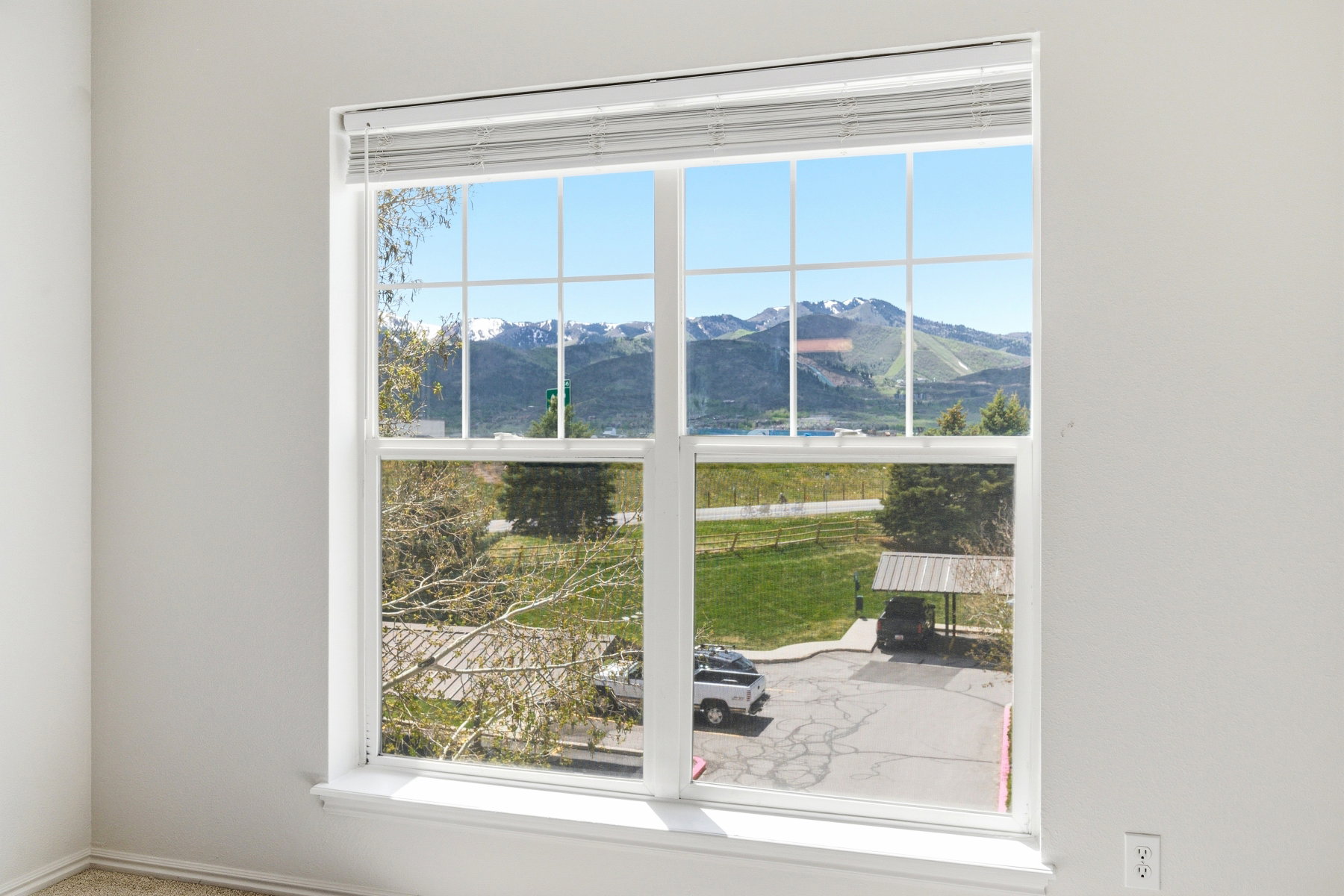Large window with white frame and grids, offering a broad scenic backdrop of snow-capped mountains and green hills