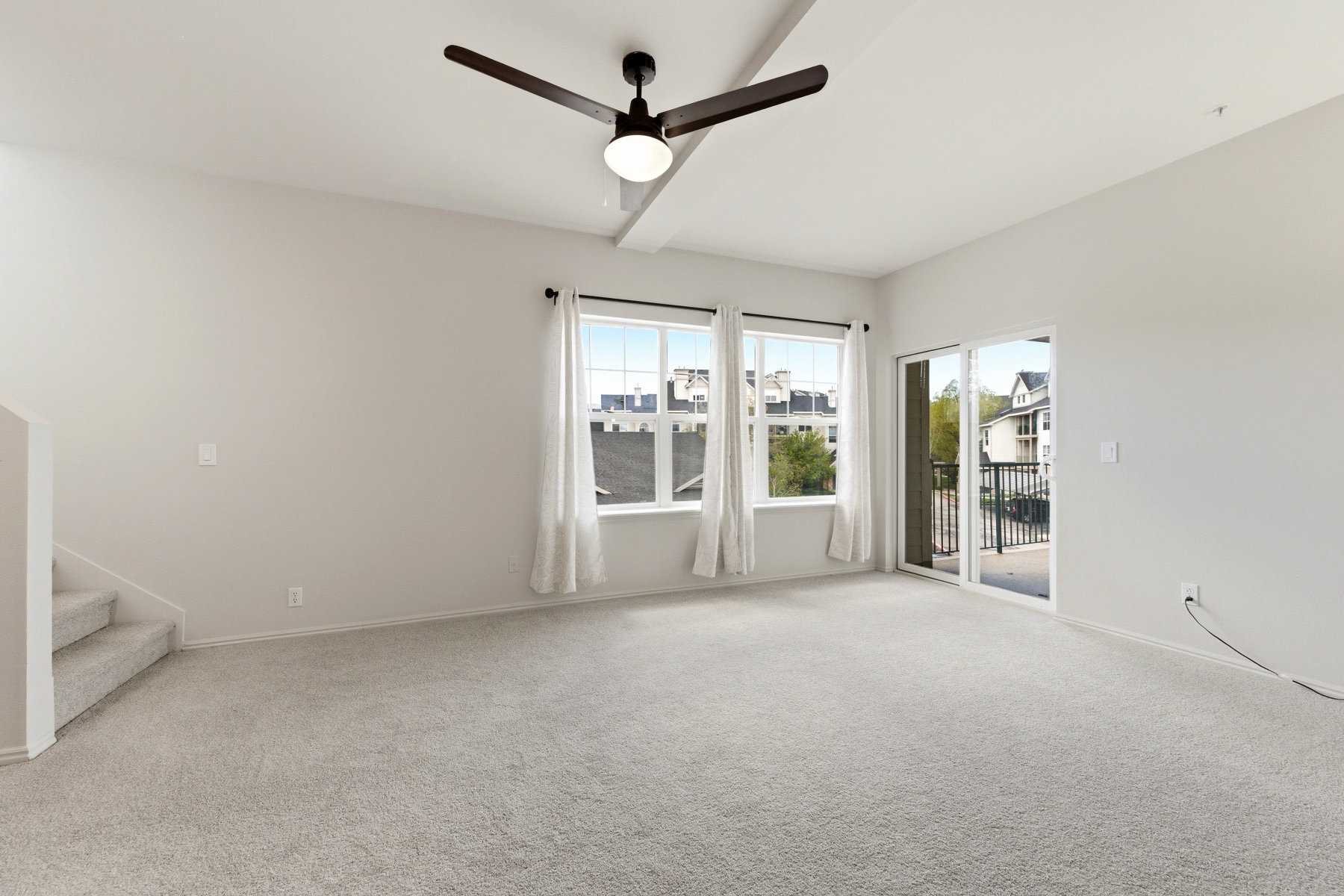 Spacious carpeted room featuring a ceiling fan with integrated lighting, multiple windows, and a sliding glass door opening to a balcony