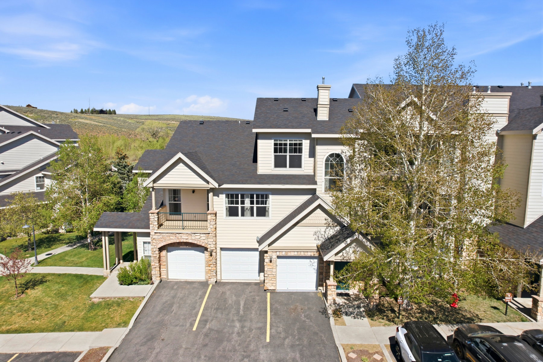 Multi-level townhome featuring a stone and siding exterior, multiple garage bays, and an upper-level balcony with a metal railing