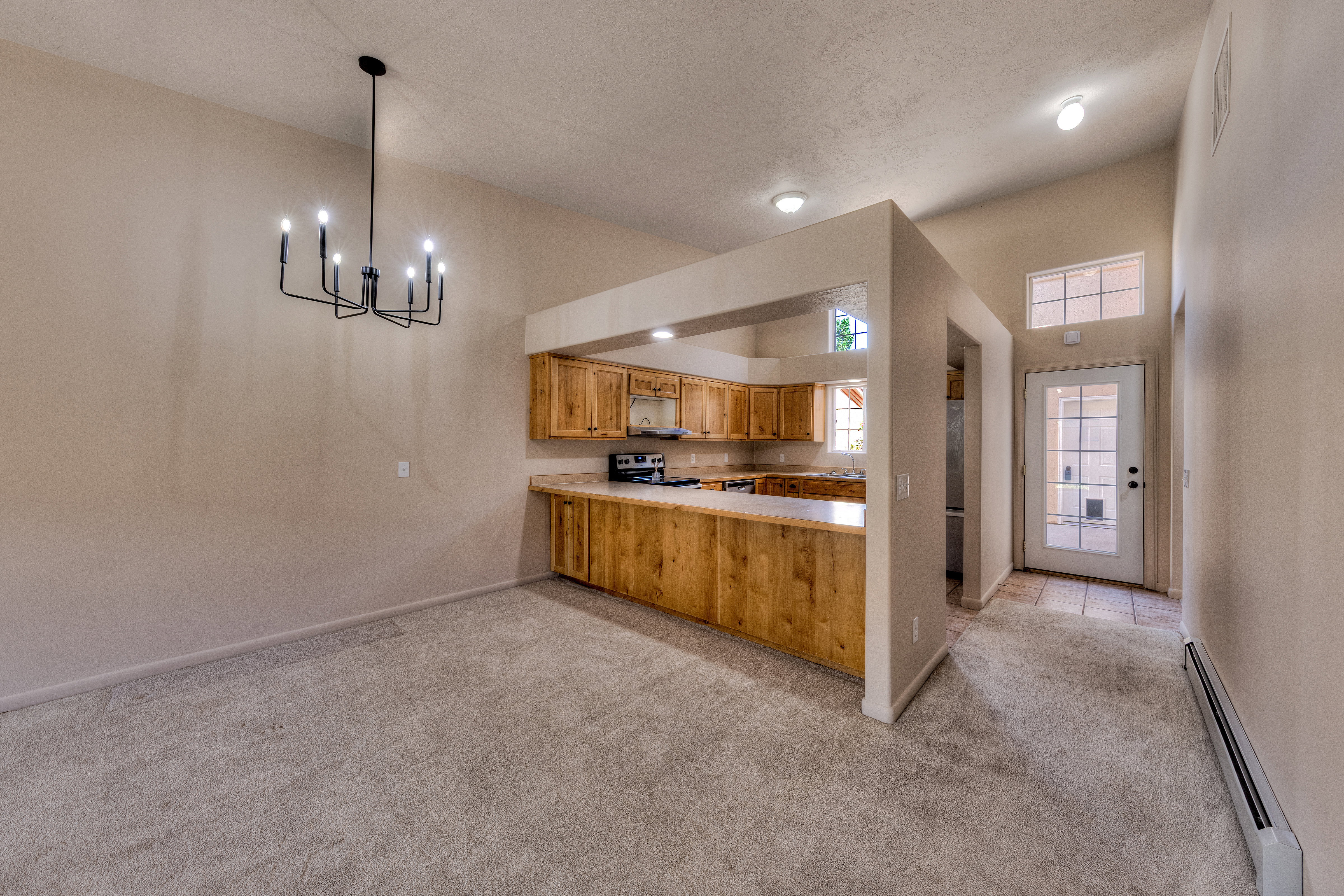Carpeted dining area featuring a black metal chandelier, vaulted ceiling, and an open concept kitchen with wood cabinetry and light countertops