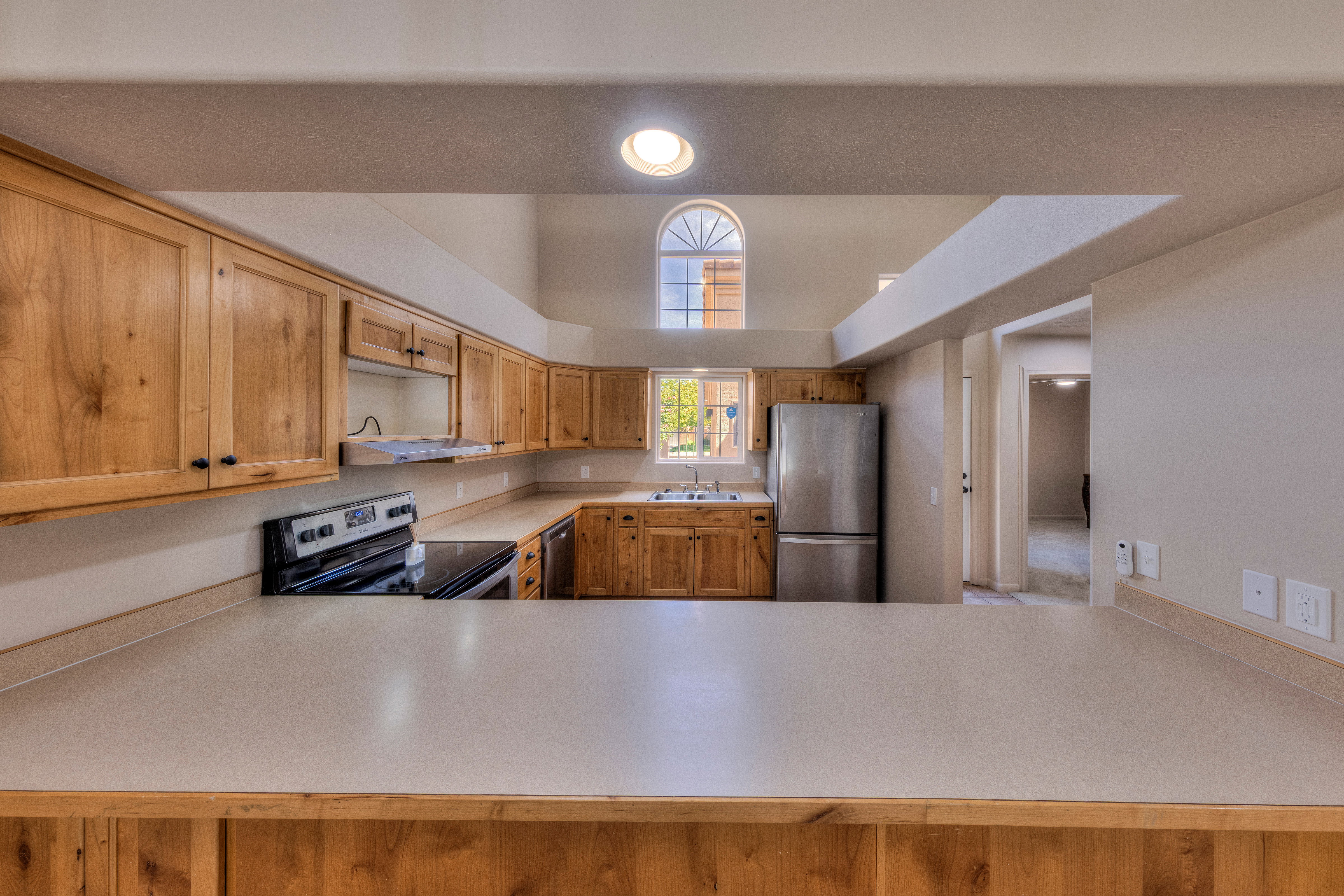 Kitchen featuring extensive wood cabinetry, light-toned countertops, stainless steel appliances, and a vaulted ceiling with an arched window