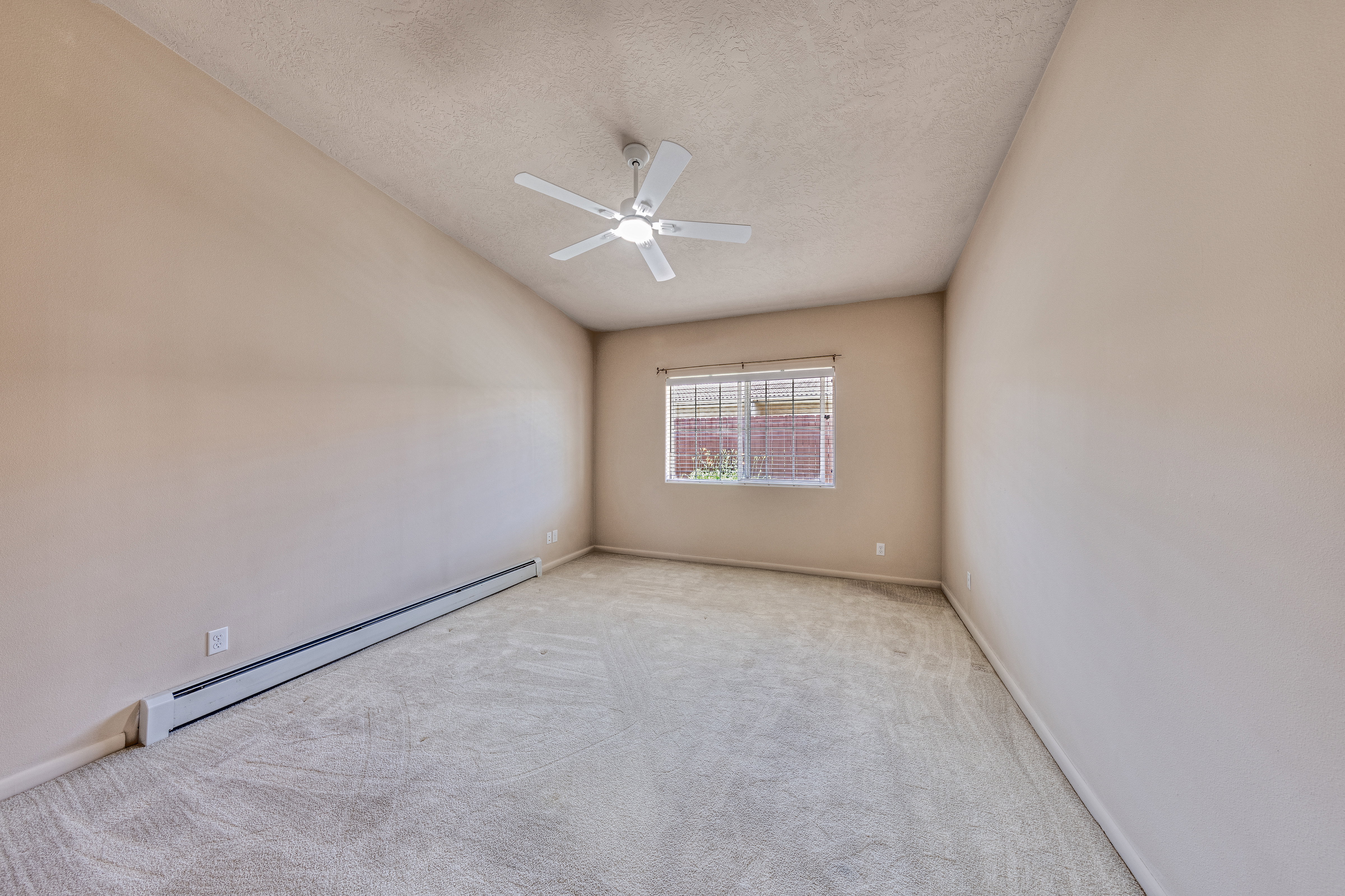 Carpeted interior space featuring a window with blinds, a ceiling fan, and baseboard heating