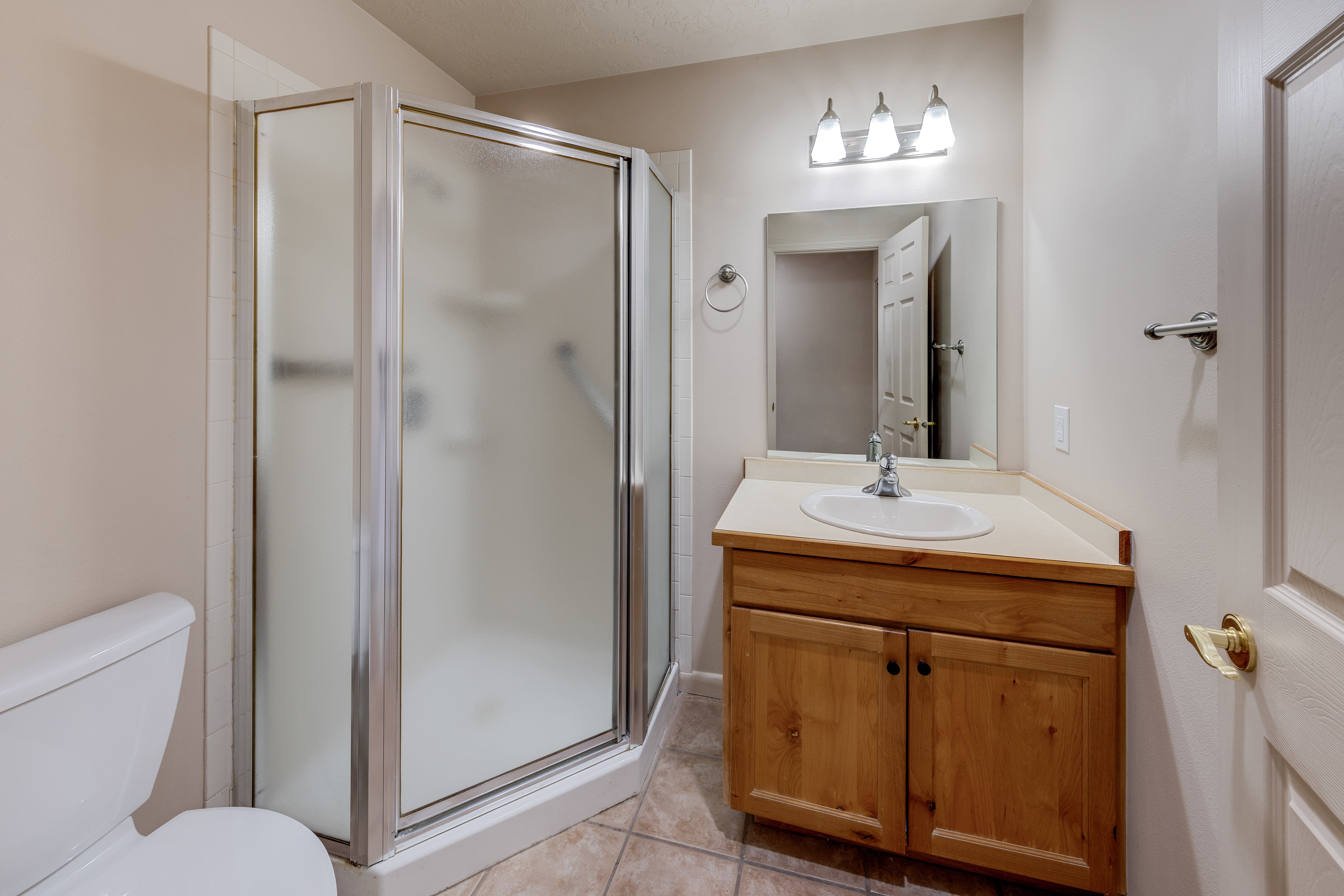 Bathroom featuring a corner shower with frosted glass enclosure, a single vanity with wood cabinetry and an integrated sink, a wall-mounted mirror, and tile flooring