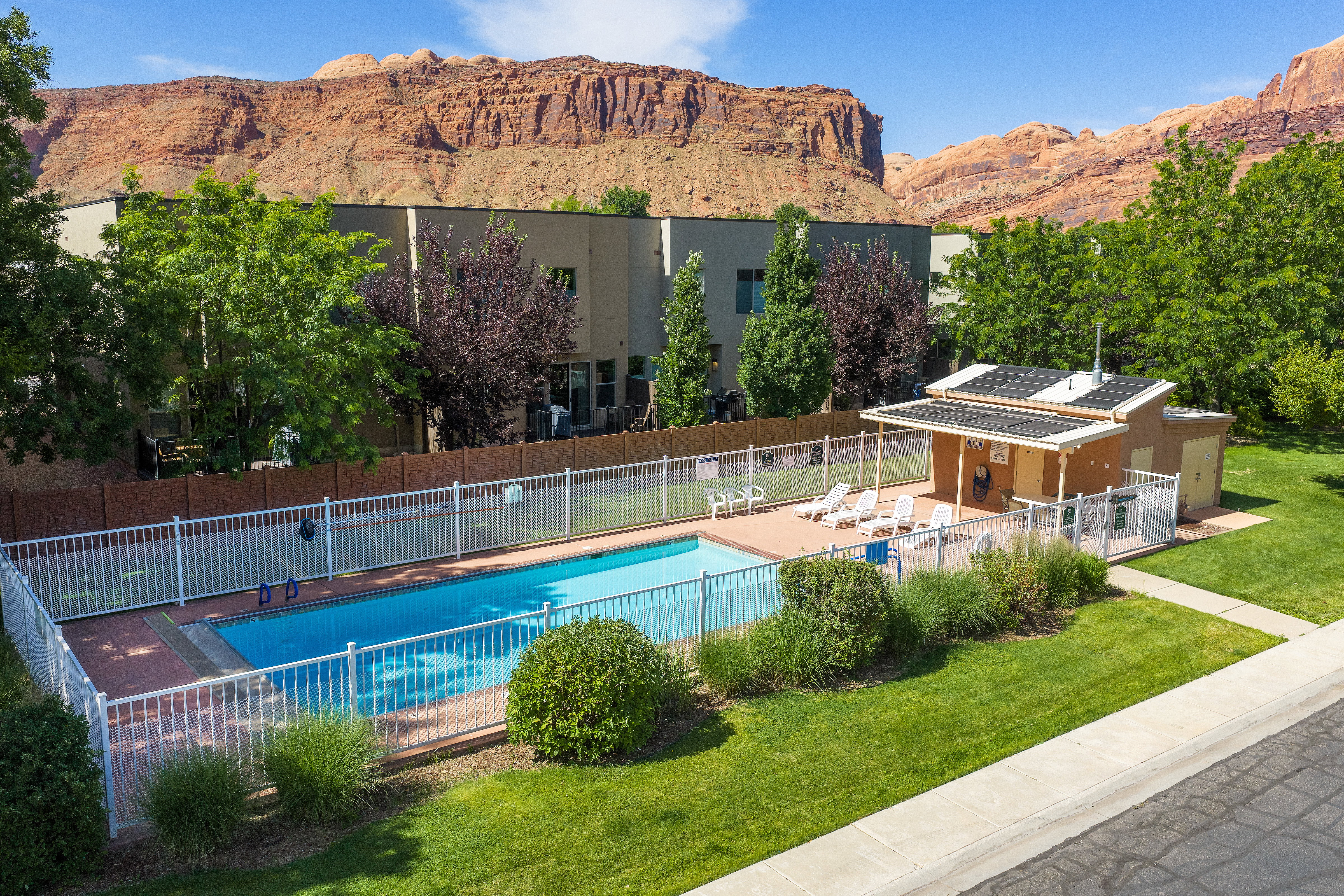Community swimming pool with a surrounding fence, adjacent pool house, and a paved sun deck