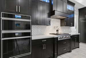 Gourmet kitchen featuring a built-in double oven, professional-grade range with pot filler, custom dark wood cabinetry, white herringbone tile backsplash, and light-toned countertops