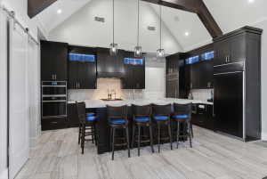 Spacious kitchen featuring dark cabinetry, a central island with countertop seating, integrated stainless steel appliances, and a herringbone tile backsplash