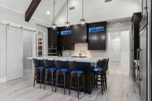 Kitchen featuring a large central island with seating, dark wood cabinetry, white herringbone tile backsplash, and integrated stainless steel appliances