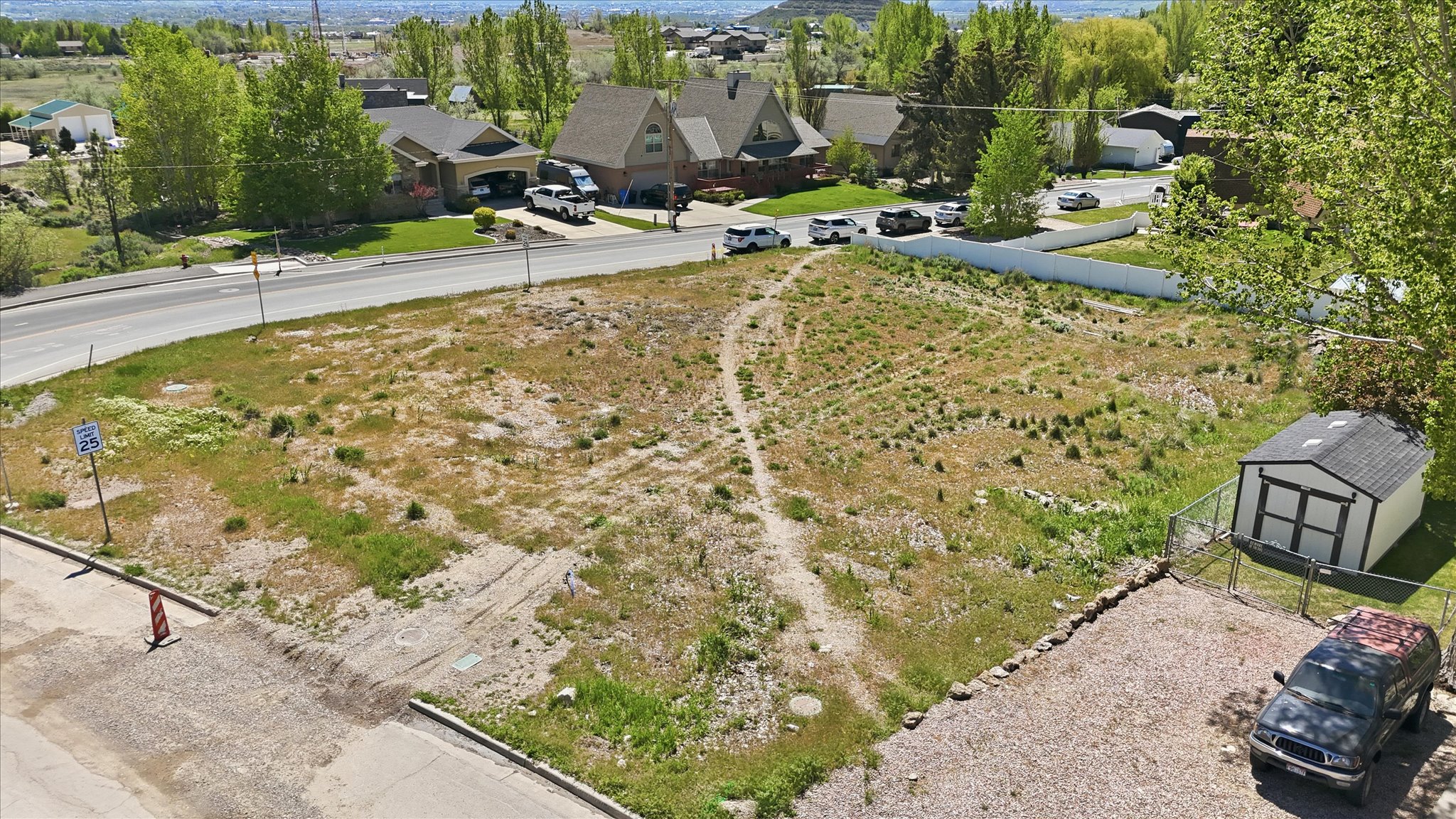Expansive land parcel featuring existing gravel parking, a storage shed, and a perimeter fence