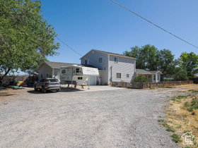 Gravel drive with ample parking, a mature shade tree, and a light-colored exterior residence