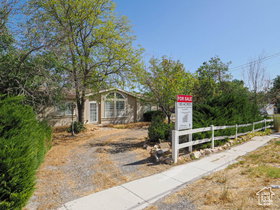 Ranch-style residence featuring a prominent arched window, mature trees, a paved driveway, and a white picket fence bordering the sidewalk