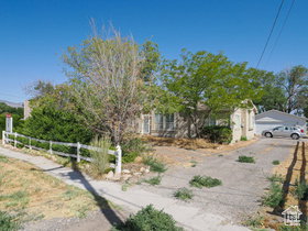 Ranch-style residence featuring a stone exterior, a white picket fence, mature trees, and a two-car garage with a paved driveway