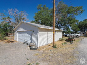 Detached garage with white siding, a single garage door, and a gravel drive