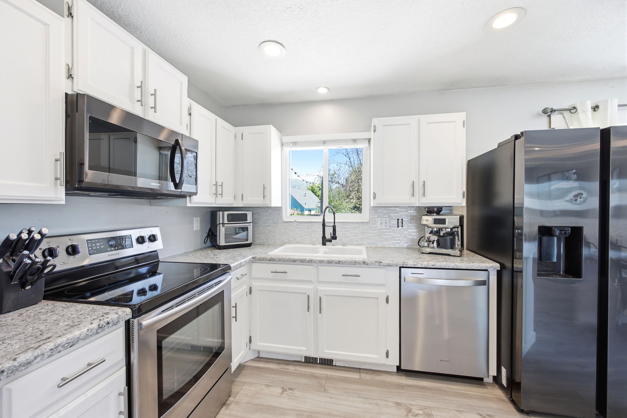 Modern kitchen featuring white cabinetry, light-toned countertops, a full suite of stainless steel appliances, and a mosaic tile backsplash