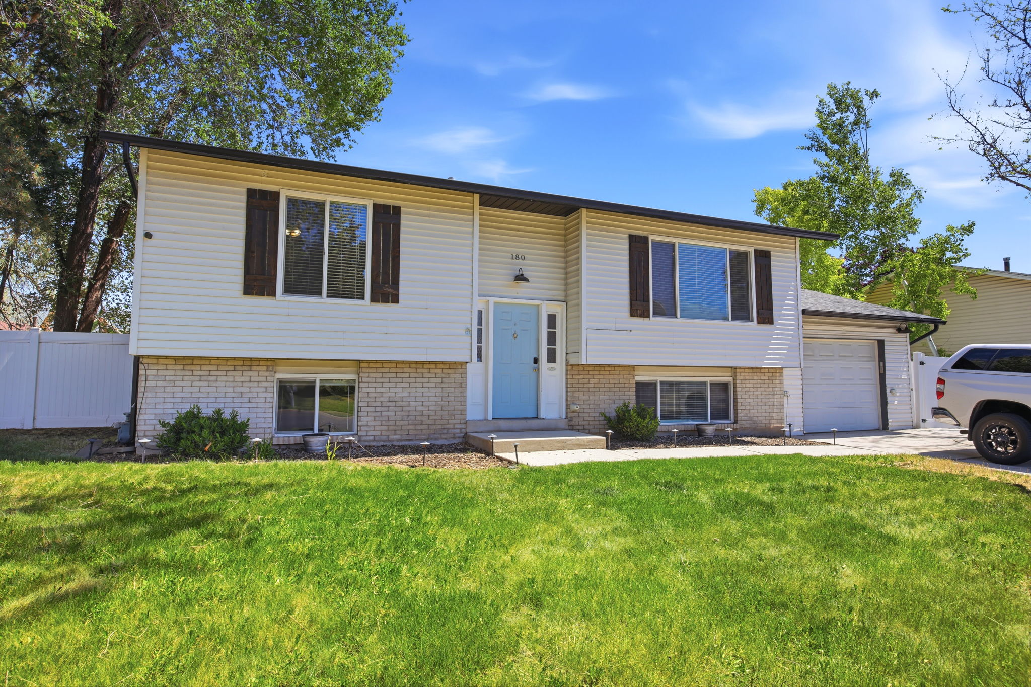 Split-level residence featuring white siding, a light blue entry door, and a white fence