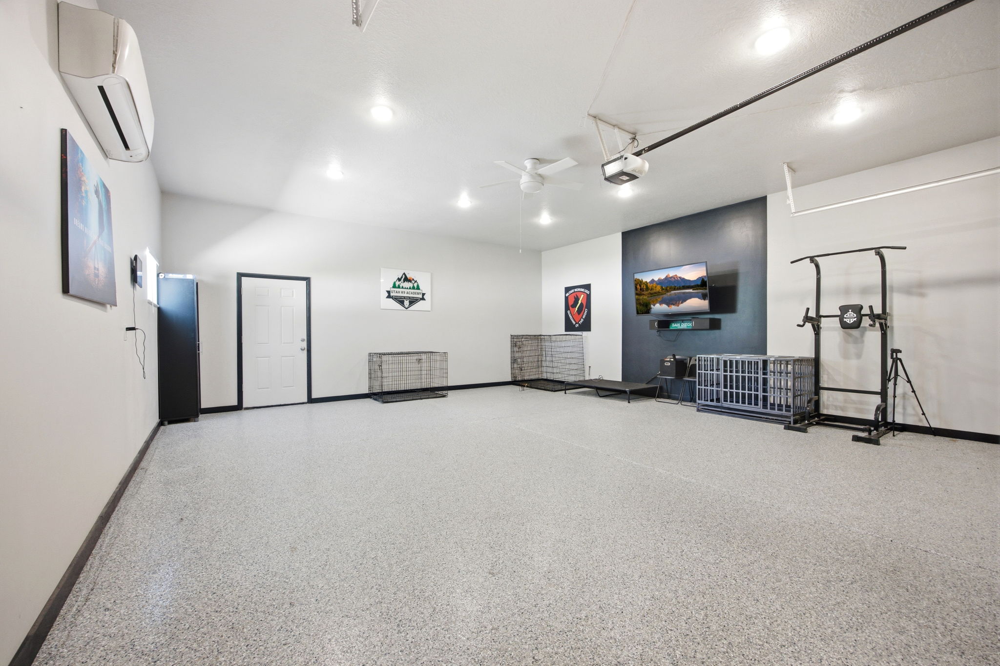 Spacious garage featuring a durable epoxy speckled floor, mini-split air conditioning unit, ceiling-mounted lighting, and a prominent accent wall with a wall-mounted television