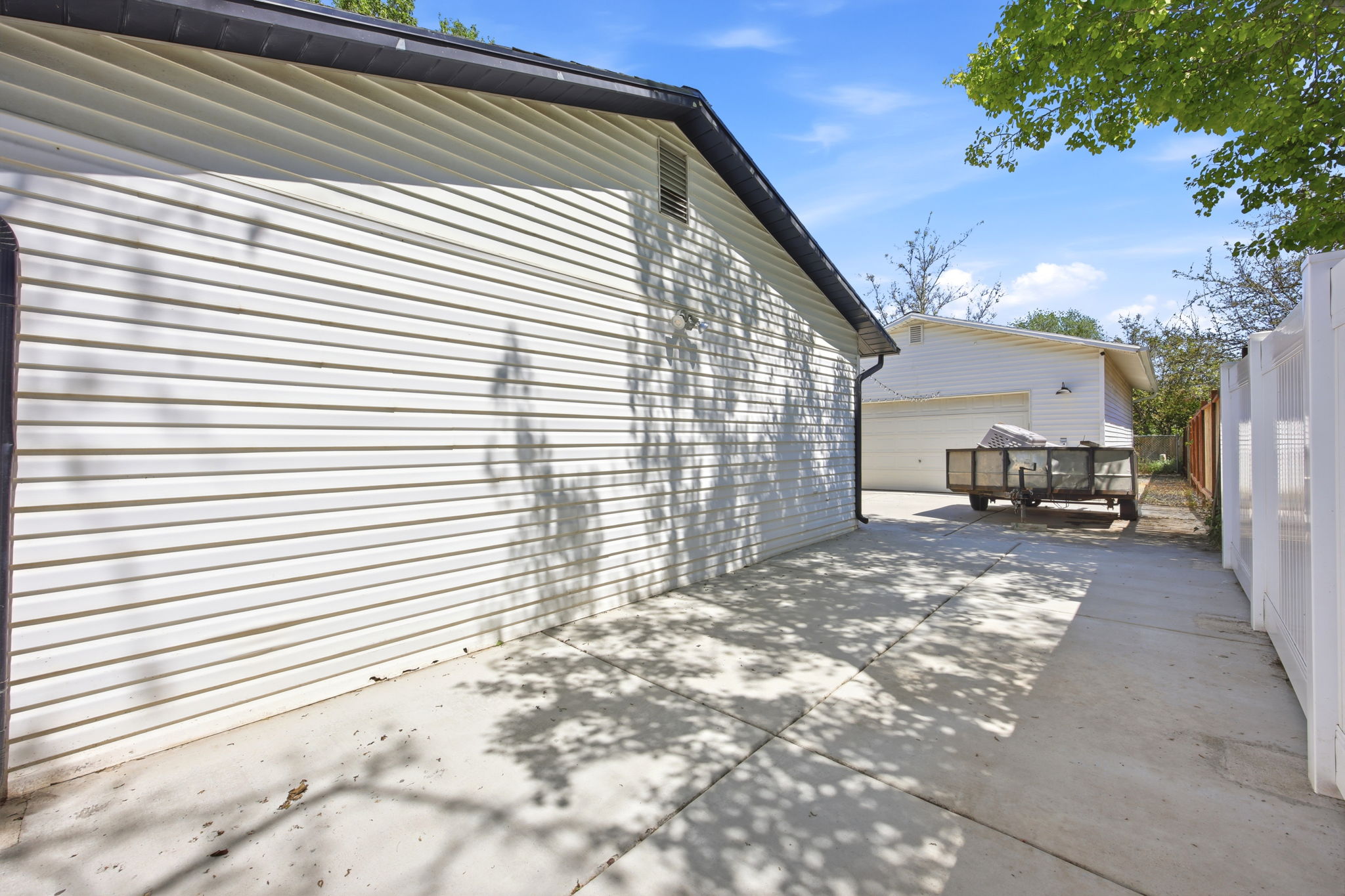Concrete driveway and white vinyl siding exterior, featuring dark soffit and fascia, with a white privacy fence