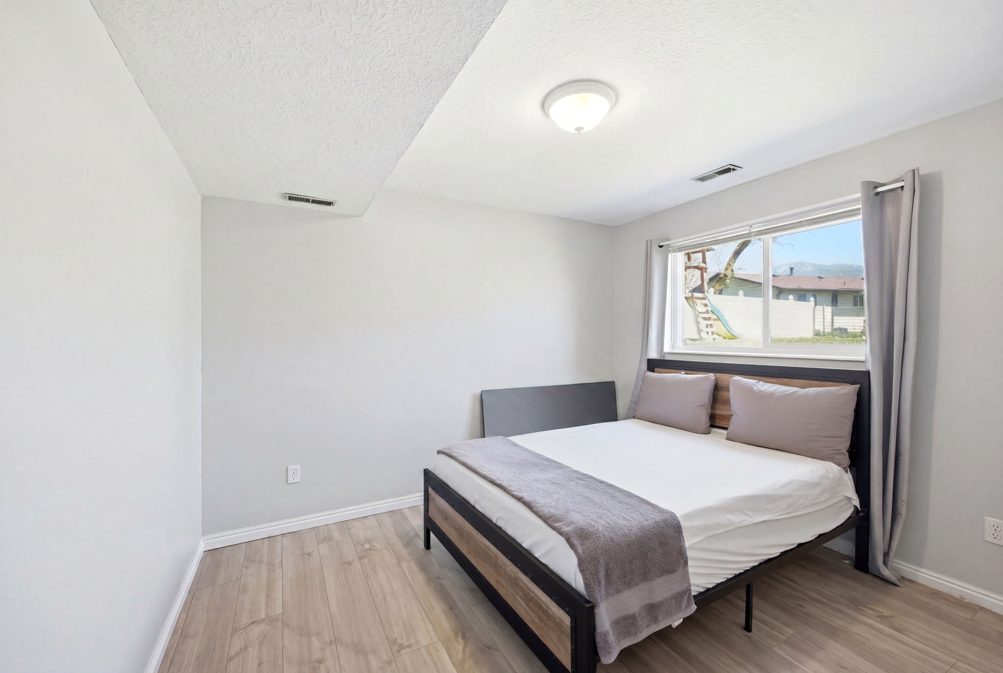 Interior room featuring wood-finish flooring, light-toned wall paint, recessed ceiling with an overhead light fixture, and a window with gray drapes