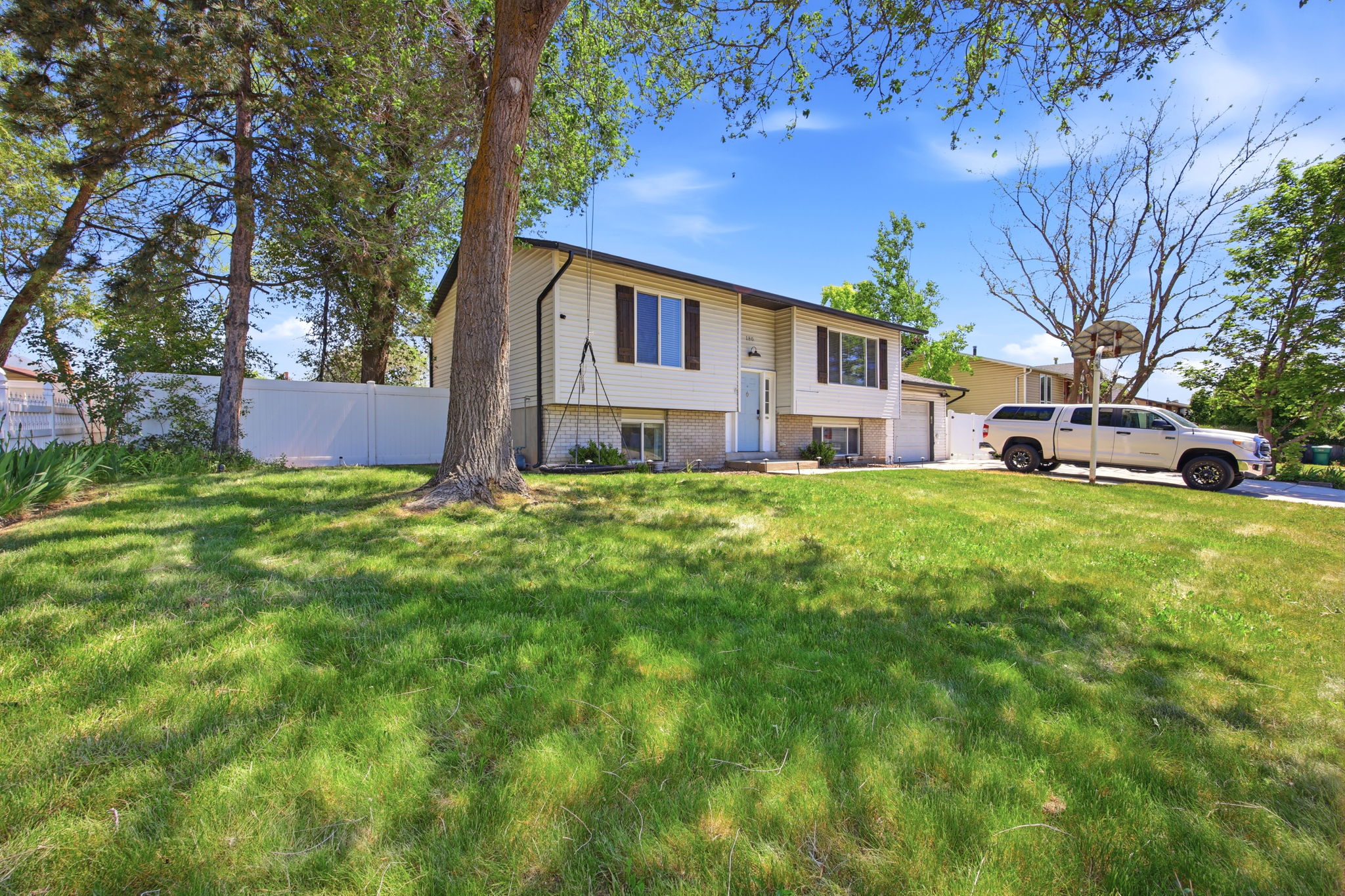 Split-level residence featuring a two-car garage, mature front yard trees, and a manicured lawn