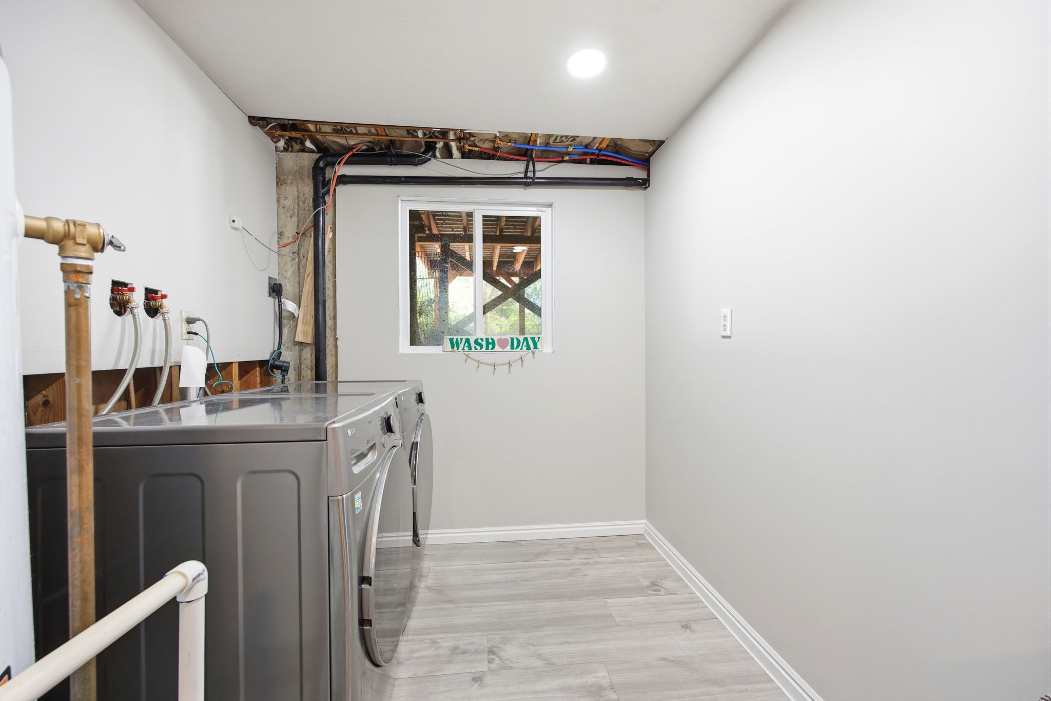 Dedicated utility space featuring light gray walls, wood-finish flooring, recessed ceiling lighting, and a single window