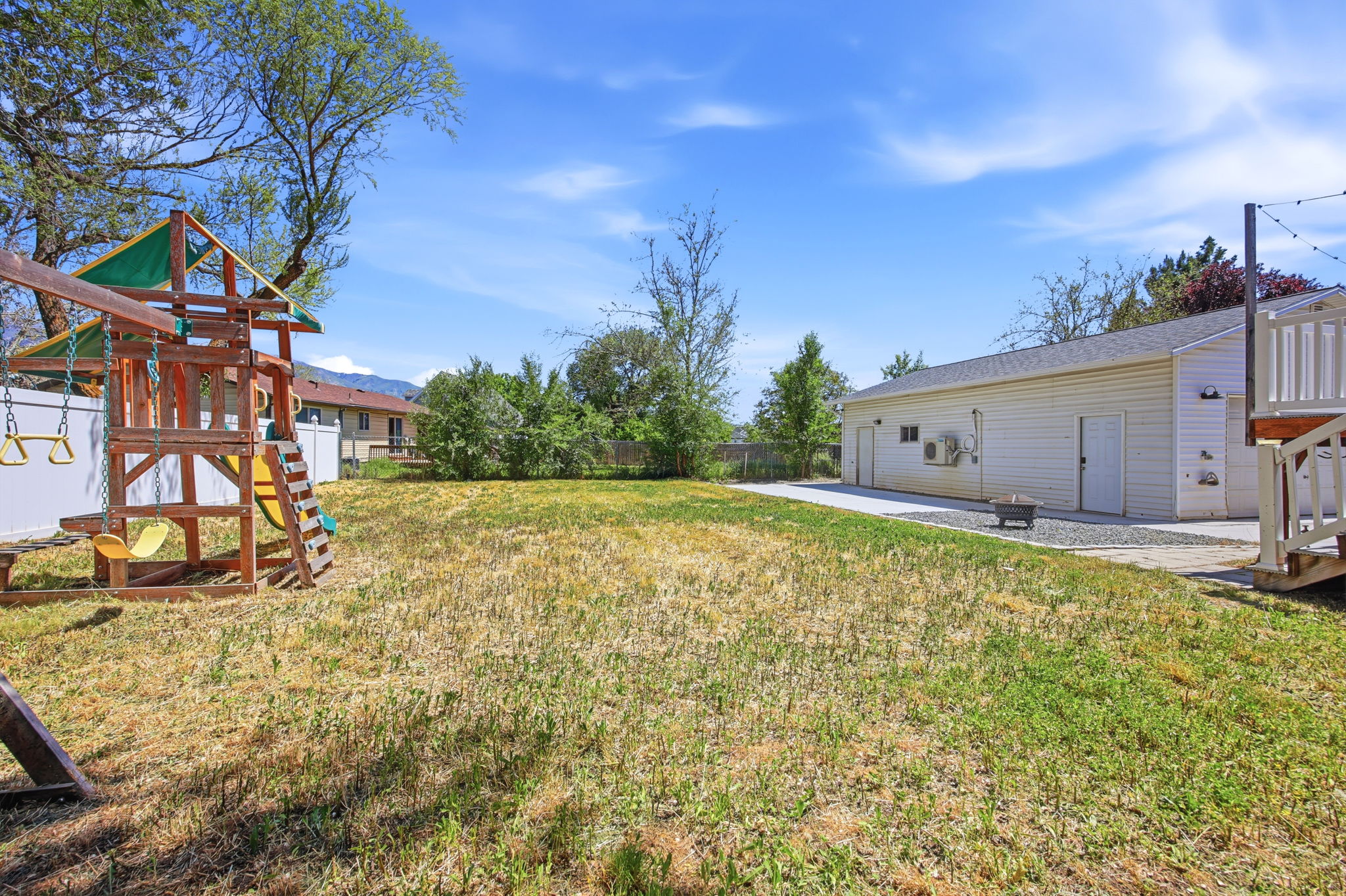 Expansive backyard featuring a large grassy area, a white vinyl fence, and a multi-purpose detached auxiliary building with multiple access points