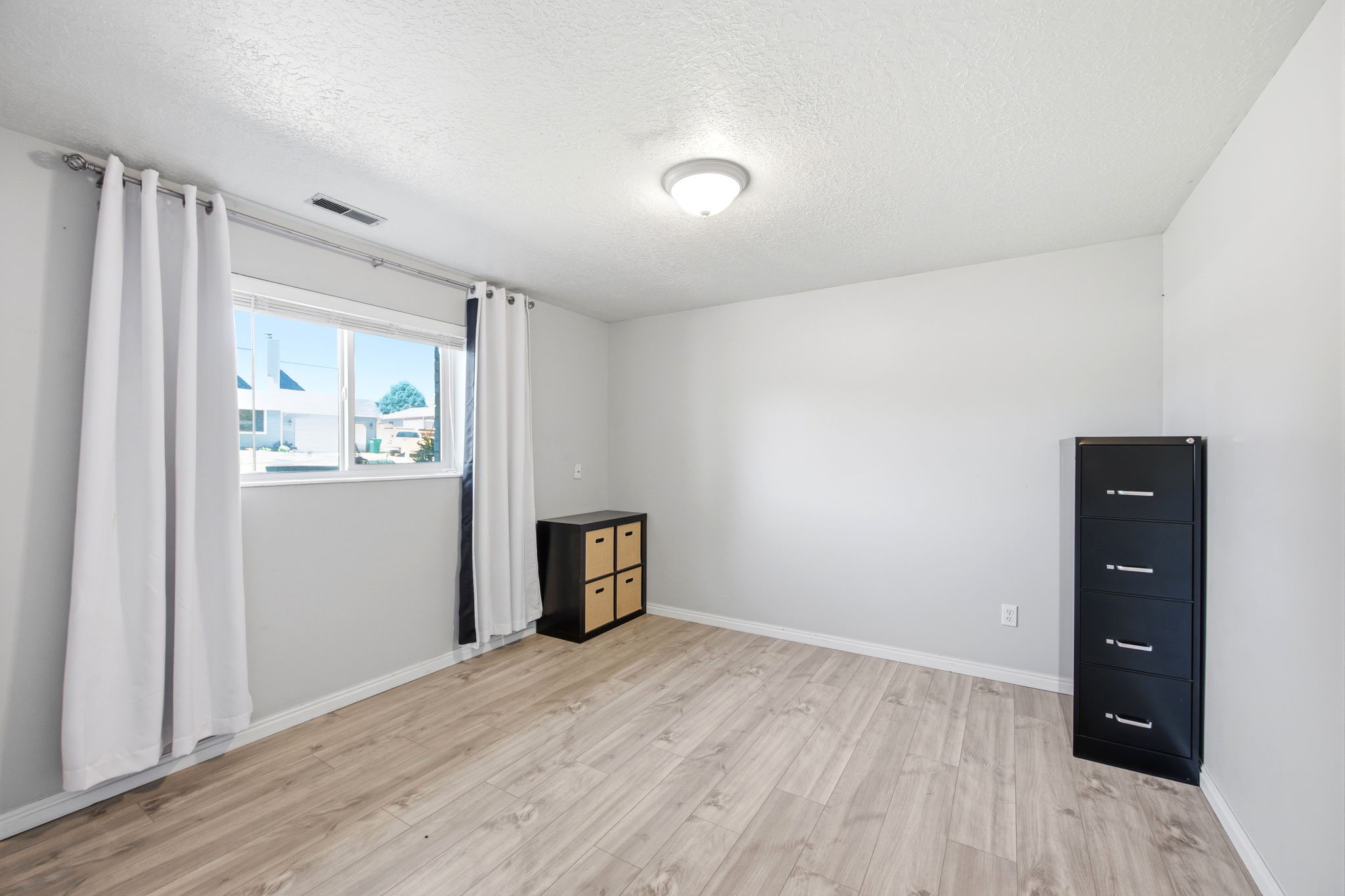 Room featuring light wood-finish flooring, white walls, and a multi-pane window