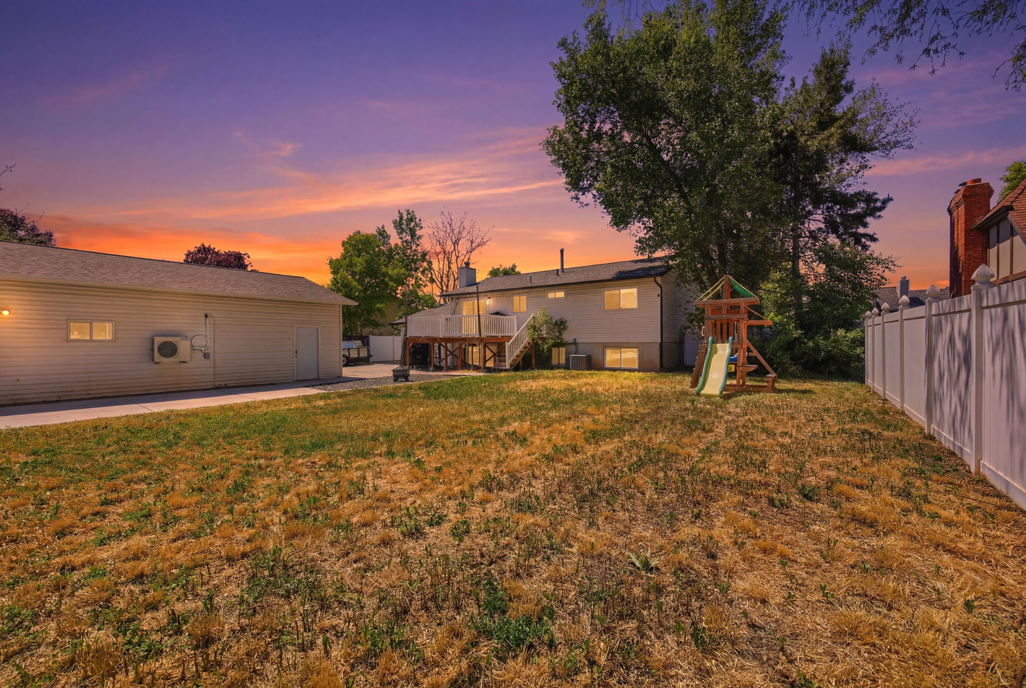 Expansive backyard featuring a large detached garage, a multi-level deck, a rear exterior with multiple windows, mature trees, and a privacy fence